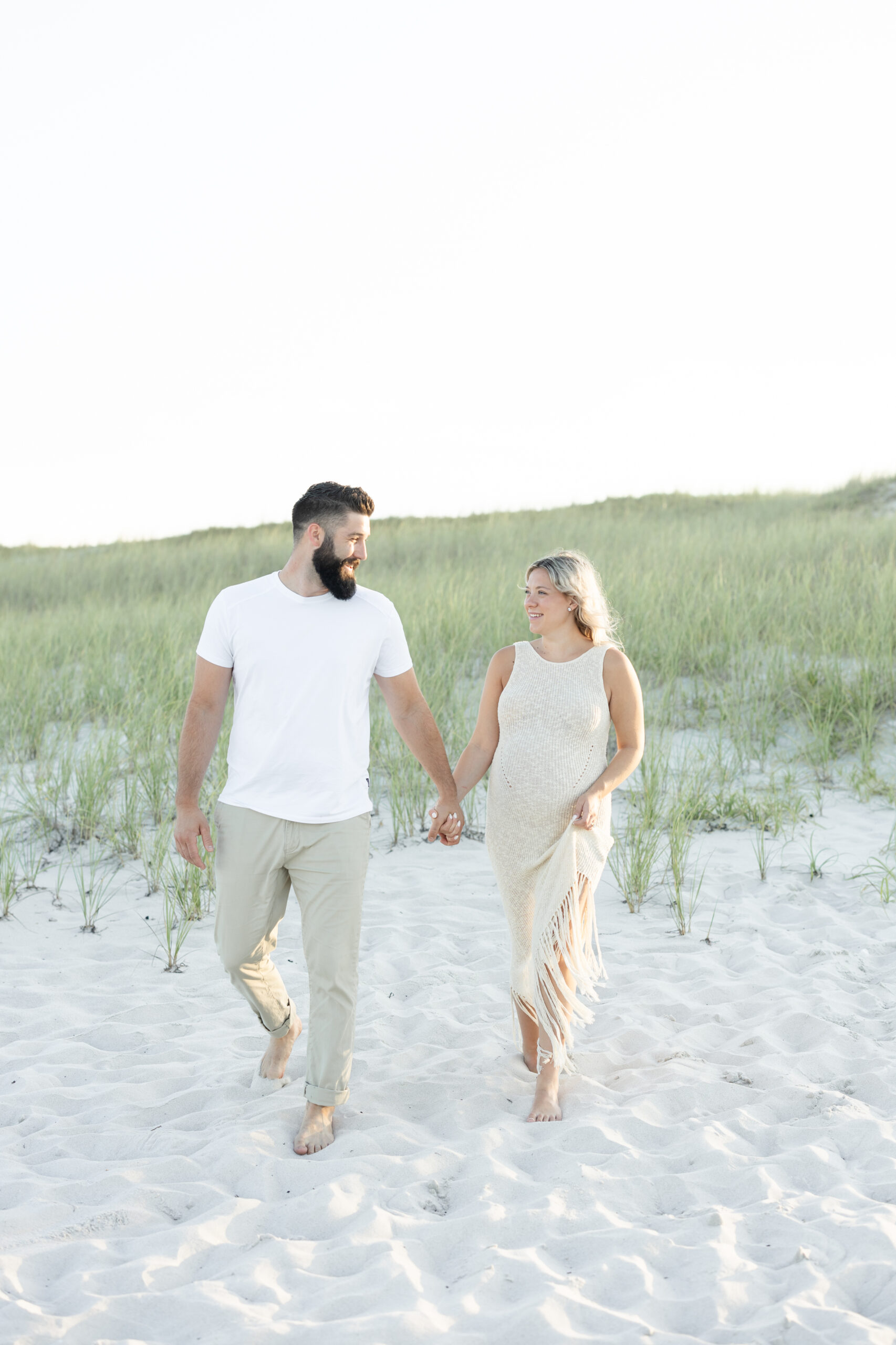 An image of a pregnant mama holding hands and walking with her husband during their maternity session on Island Beach State Park. She was photographed by Natalie Beach Photography, a South Jersey Family Photographer.