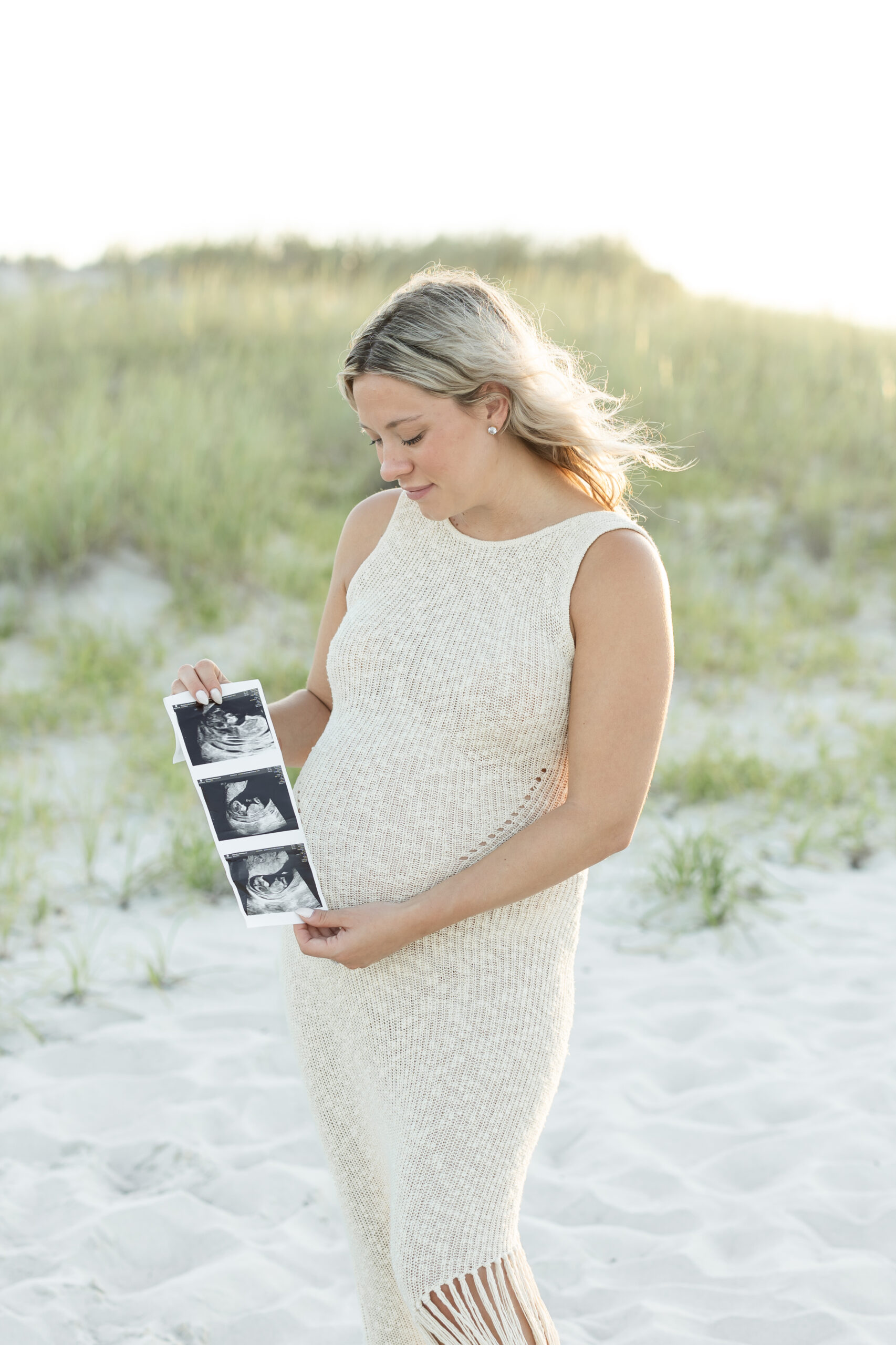 An image of a pregnant mama during her maternity session on Island Beach State Park. She is holding her ultrasound pictures. She was photographed by Natalie Beach Photography, a South Jersey Family Photographer.
